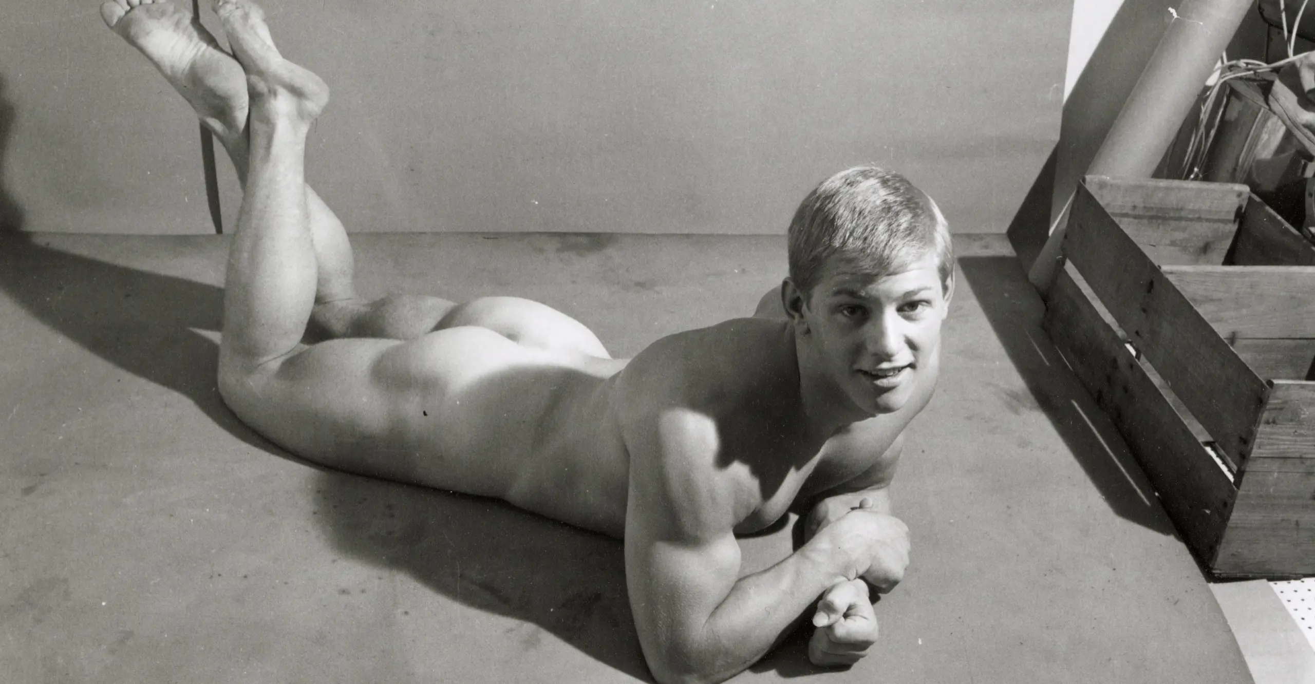 B&W photography of a white male figure laying on floor on stomach looking at camera